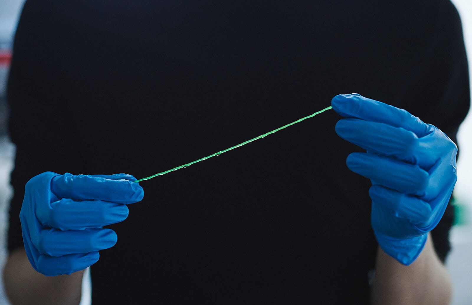 An image of two blue-gloved hands holding a green strand of Werewool's thread. Photographed by Jon Brown.
