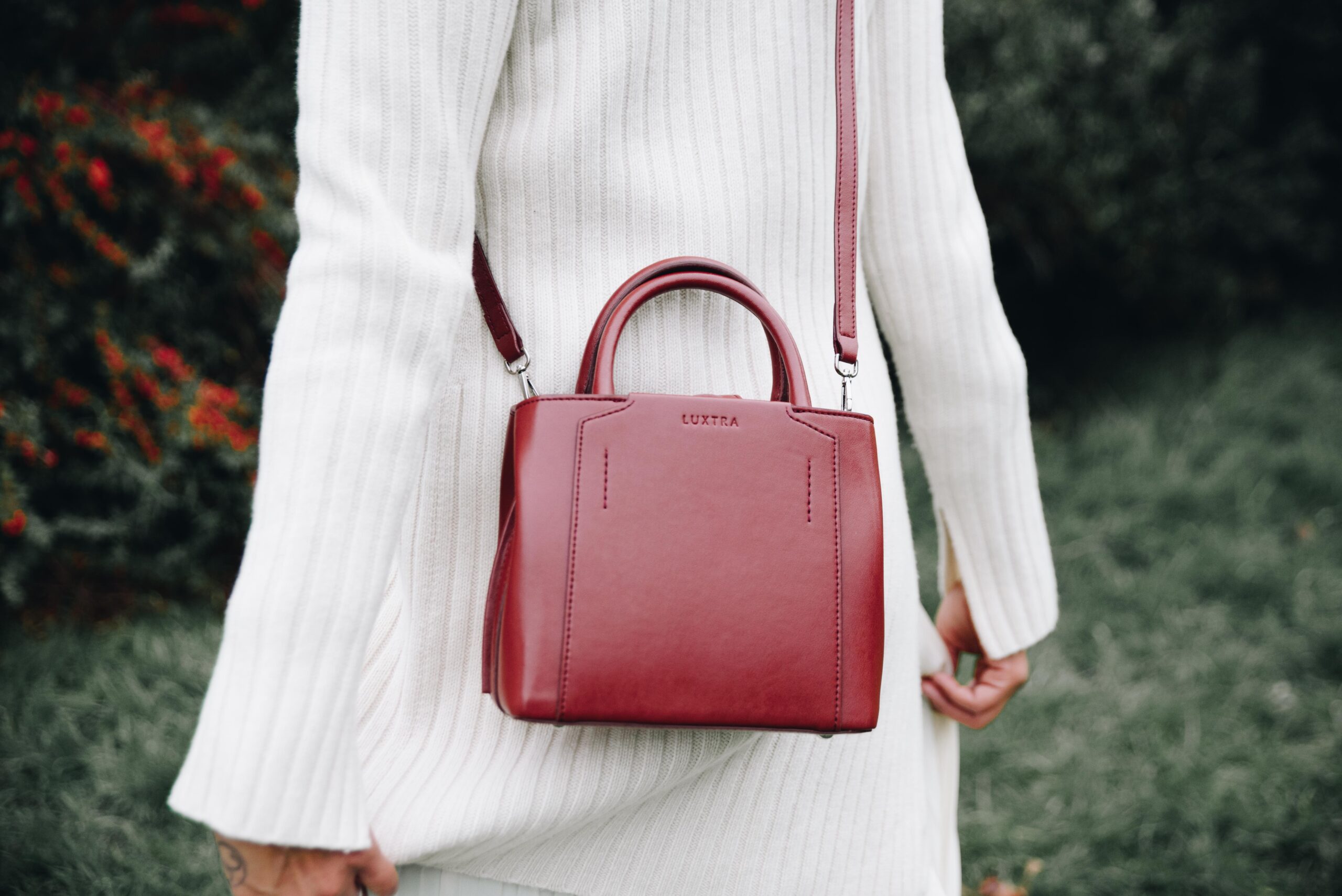 A person in a white knitted dress wearing a small red Desserto leather purse on their back, made by LUXTRA.